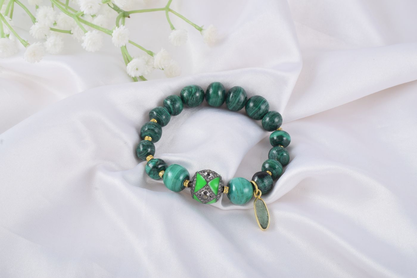 A dark green stone bracelet with gold details on white silk fabric